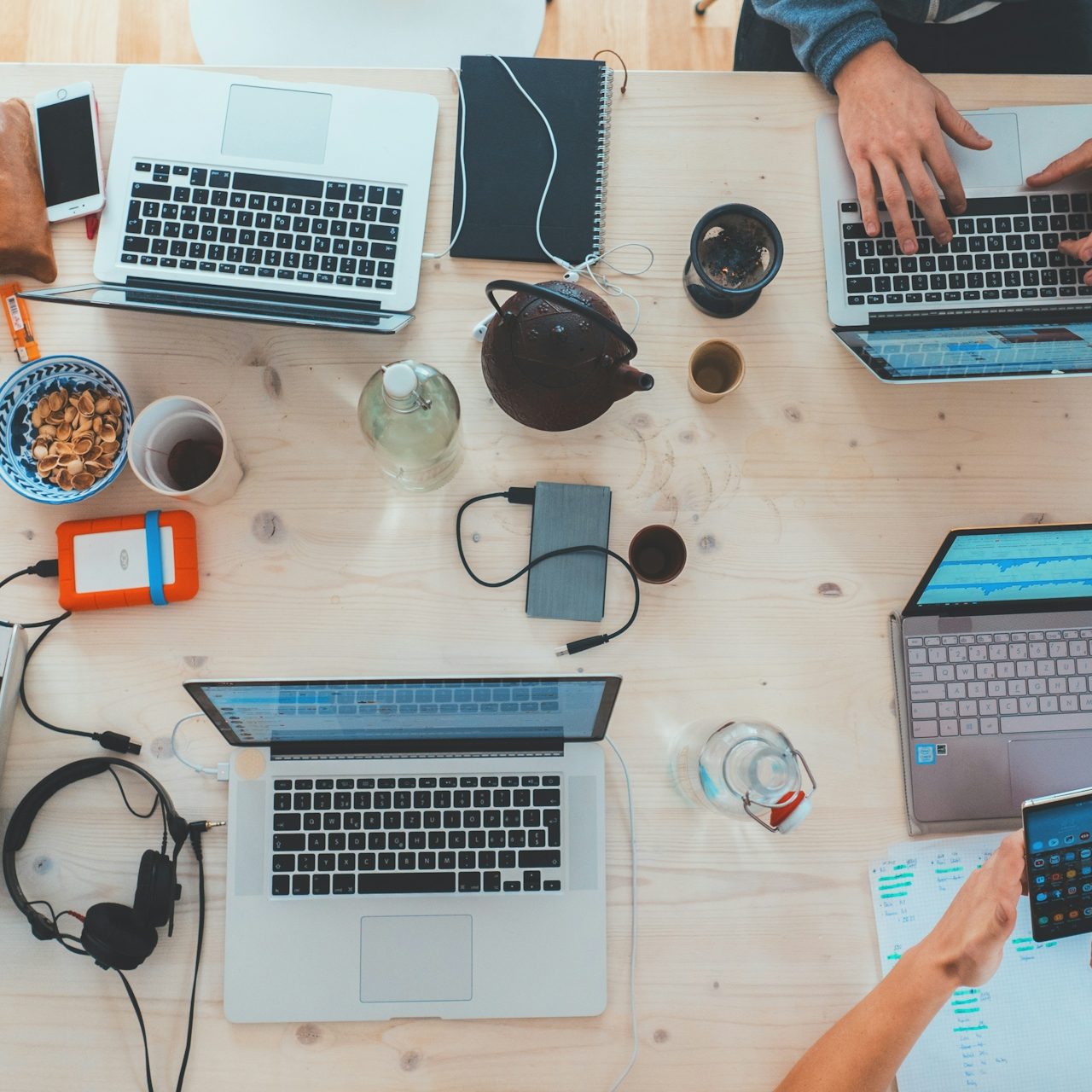 Laptop-Arbeitsplatz mit Getränken, Snacks und Personen, die an verschiedenen Geräten tippen.