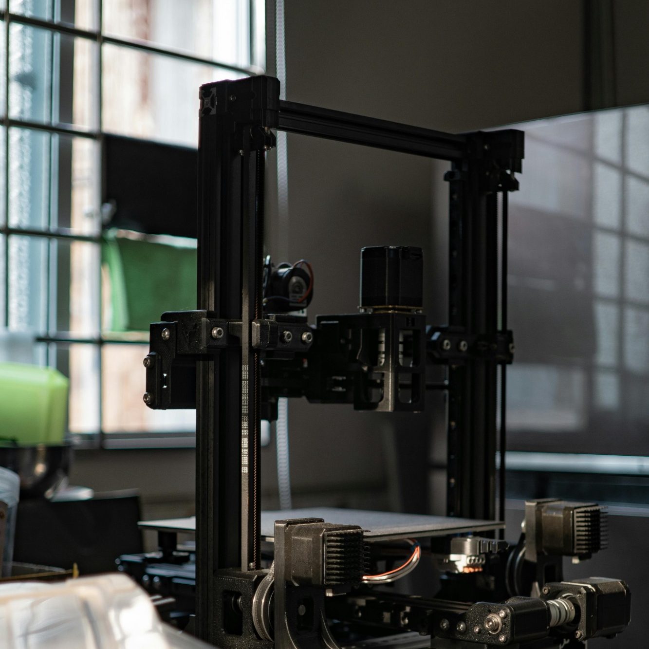 Ein 3D-Drucker steht in einem Raum mit Fenster und grüner Tischlampe.
