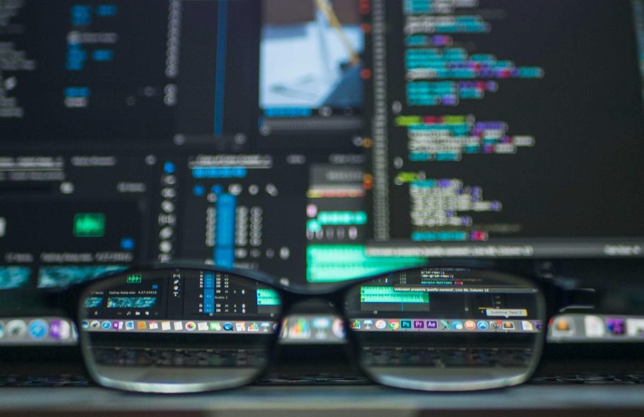Brille liegt auf einem Laptop mit Programmiercode und Softwareoberflächen.